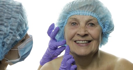 Smiling elderly female in protective hat. Plastic surgeon checking woman face