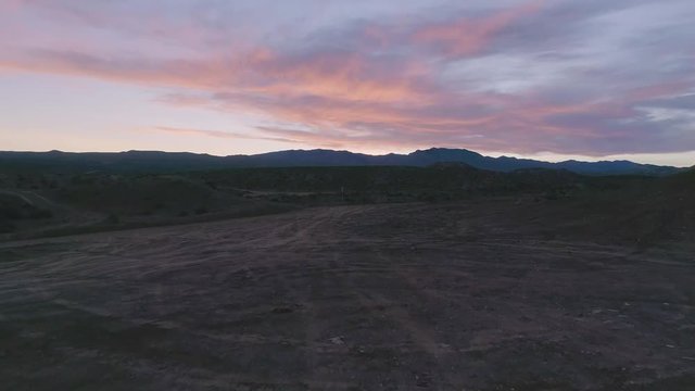 Drone shot tracking along brush and winding desert roads with late colorful sunset and mountains in background.  Springtime.
