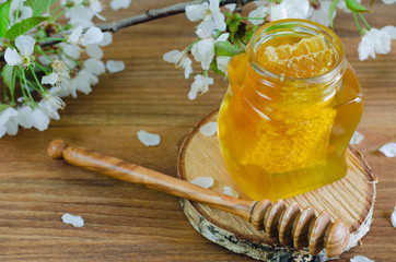 Honey jar with honeycomb and honey dipper on wooden background with cherry blossoms.