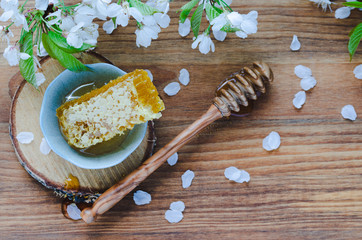 Honeycomb in ceramic bowl and honey dipper on wooden background with cherry blossoms.