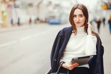Beautiful girl standing in a autumn city. Lady with a tablet. Woman on the street