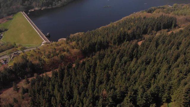 Drone travelling away from Lady Bower Reservoir Whilst panning up revealing Lady Bower Reservoir from a Forest near by towards Bamford Edge in the Peak District shot in 4K