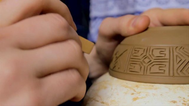 Engraving, shaping a new pottery item. Close up of hands writing on pottery.