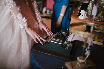 Bride in a white wedding dress works on a typewriter