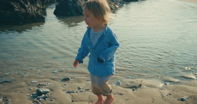 Happy little toddler walking on the beach in summer at sunset