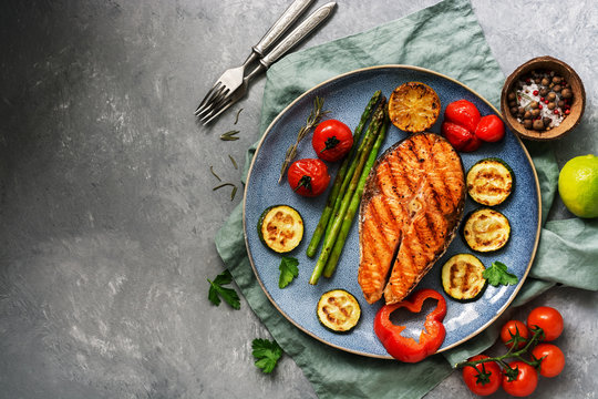 Grilled salmon with vegetables zucchini, asparagus, tomato, sweet pepper on a plate, gray background. Top view, flat lay,copy space