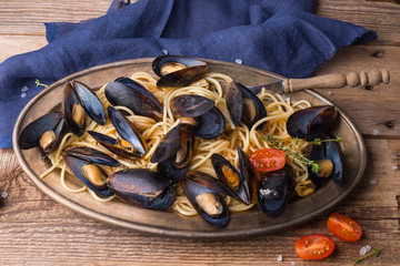 Spaghetti with mussels, tomatoes in spicy sauce in the original plate on the old wooden table. Clams Mytilus closeup. Italian pasta. A dish for a romantic dinner.