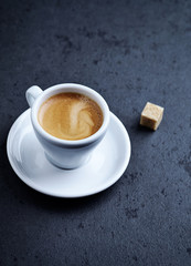 Cup of coffee and a brown sugar cube on dark stone background. Copy space