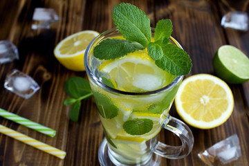 Cold  lemonade with lemon and mint  in the glass on the brown wooden background.Closeup.