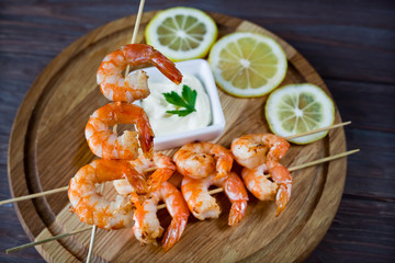 fried shrimps on a skewer in hand against the background, shrimp kebab on a wooden board with parsley and lemon out of focus