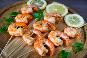fried shrimp on skewers, skewers, on a wooden board with parsley and lemon, closeup