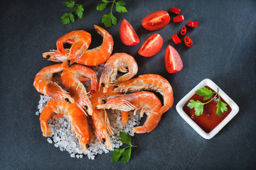 boiled shrimps on dark gray background with sauce and tomatoes and parsley, top view