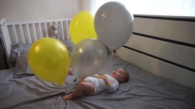 A little baby is playing with four ballons on the bed