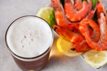 a glass of beer with foam on the background of boiled shrimps with lemon out of focus on the table