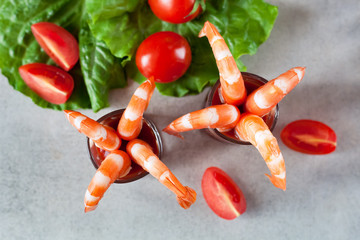 Shrimp cocktail in small glasses, with cherry tomatoes, lettuce, top view on a light gray table