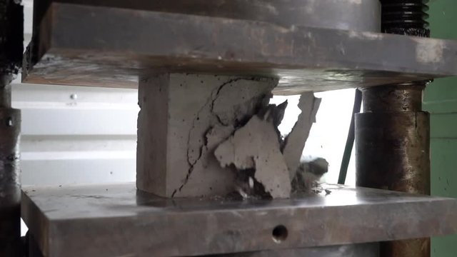 Concrete cube test. Concrete under pressure in hydraulic press. How strong is concrete. Load durability test. Cracks in concrete.