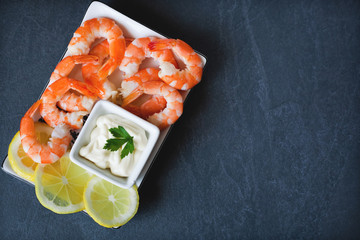 cooked peeled shrimps in a plate with lemon and white sauce on a dark table, with a place for the inscription