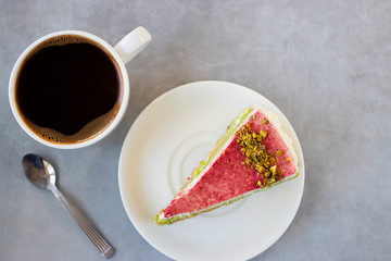 A piece of pistachio cake on a white plate and a cup of coffee.