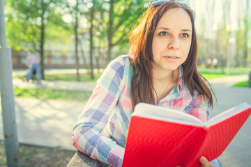 Woman with a book in his hands in the Park. Female, student is reading an interesting book sitting on the bench in the park