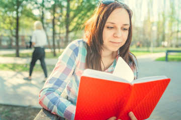 Obraz premium Woman with a book in his hands in the Park. Female, student is reading an interesting book sitting on the bench in the park