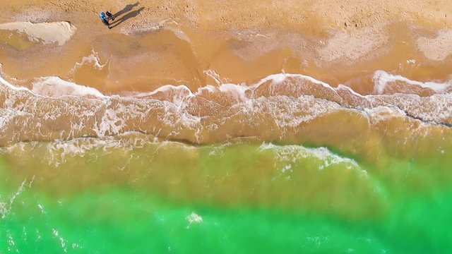 Top view of a superb lonely and deserted beach on the shores of the azure sea. Dawn of nature in 4K. A bird's eye view of ocean waves crashing against an empty beach from above