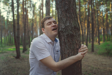 Man hugging tree in the forest. Smiling young male nature lover relax on summer day hug a tree...