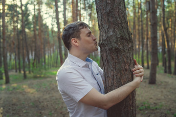 Man hugging tree in the forest. Smiling young male nature lover relax on summer day hug a tree enjoy in beautiful day	