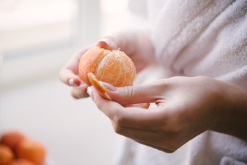 Woman cleans the tangerine with hands close up