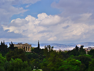 Fototapeta na wymiar Temple of Hephaestus in Athens, Greece. Landscape with olive, cypress and other trees cloudy sky, bright light, and ancient greek temple.