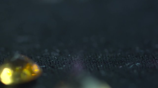 Macro shot of precious gems diamonds and zircons made with a Red camera on slow motion falling on a black background inside a jewelry workshop