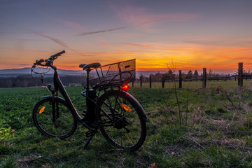 Fototapeta premium Black electric bicycle with sunset on light green meadow in spring evening