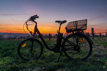 Fototapeta na wymiar Black electric bicycle with sunset on light green meadow in spring evening