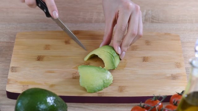Female hands slicing avocado for sandwich.