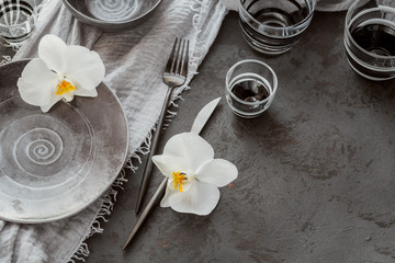 Elegance table setting with knitted grey napkin, cutlery, ceramic plates, glasses and white orchid flowers