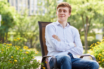 Young attractive man in white shirt sitting on brown chair in the park on green background - 264466267
