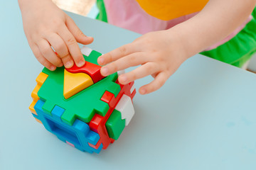 close-up of the child's hands collect puzzle sorter. Cube with inserted geometric shapes and colored plastic blocks.