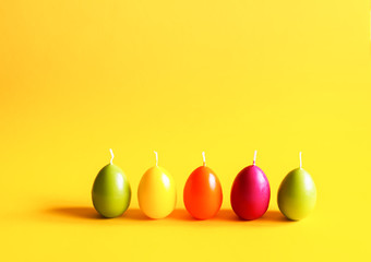 Traditional Easter decor. Group of bright burning paraffin candles in the shape of colorful eggs on...