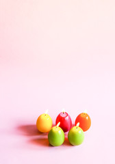 Traditional Easter decor. Group of bright burning paraffin candles in the shape of colorful eggs on pink background.