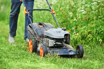 European man is mowing the lawn on his countryside plot. © Artem