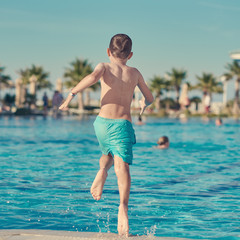 Caucasian boy having fun making jump into swimming pool at resort. Back view. - 264467884