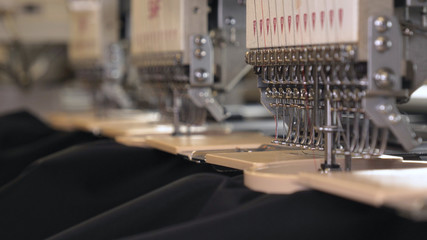 In slow motion video in a garment factory, a sewing machine embroiders various companies and...