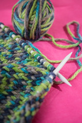 Skein of thread and knitted fabric on a pink background.