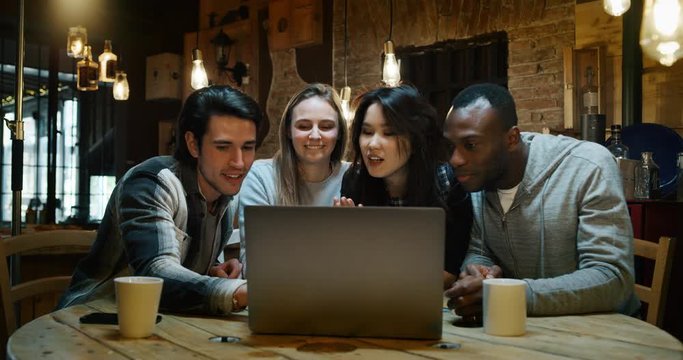 Slow motion of young college friends using a laptop together for study project and drinking tea in a cafe. Shot in 8K. Concept of student life, education, technology, teamwork
