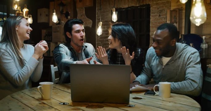 Slow motion of young college friends using a laptop together for study project and drinking tea in a cafe. Shot in 8K. Concept of student life, education, technology, teamwork