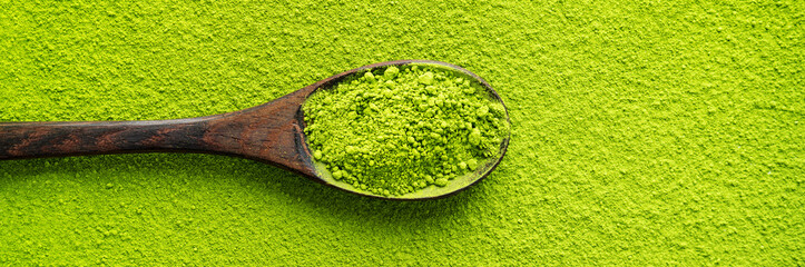 Top view of wooden spoon with green tea Matcha on powder maccha texture background. Long wide...