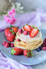 Fritters with strawberries, blueberries and raspberries on a gray plate front view against the background of a concrete wall and pink flowers