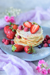 Fritters with strawberries, blueberries and raspberries on a gray plate close-up front view against the background of a concrete wall and pink flowers