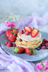 Fritters with strawberries, blueberries and raspberries on a gray plate close-up front view against the background of a concrete wall and pink flowers