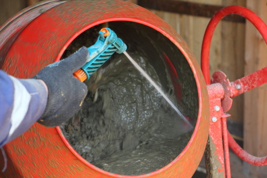 Worker washes red concrete mixer with a stream of water