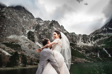 Naklejka premium Beautiful wedding photosession. The groom circles his young bride, on the shore of the lake Morskie Oko. Poland